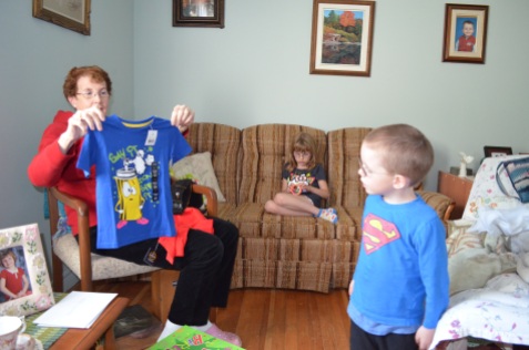 Grandma showing Aiden his new t-shirt, while Abby plays with Slinky on couch.