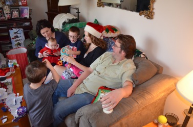 Melissa holding Eva, Aiden, Julie, Peter and Macklan opening presents.
